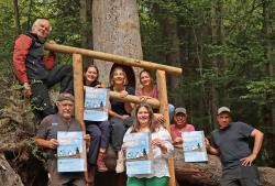 Das Organisationsteam des Spechtfests nimmt schon mal die diesjährigen Plakate zur Hand, um vor der Spechthöhle des Waldspielgeländes die Werbetrommel zu rühren. (Foto: Nationalpark Bayerischer Wald)